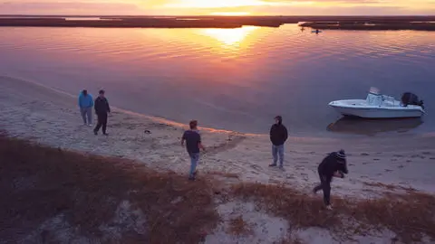 Guests on a sandbar next to an anchored boat at sunset